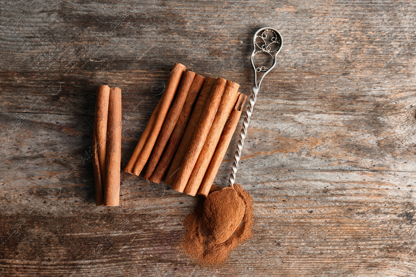 Photo of Spoon with aromatic cinnamon powder and sticks on wooden background