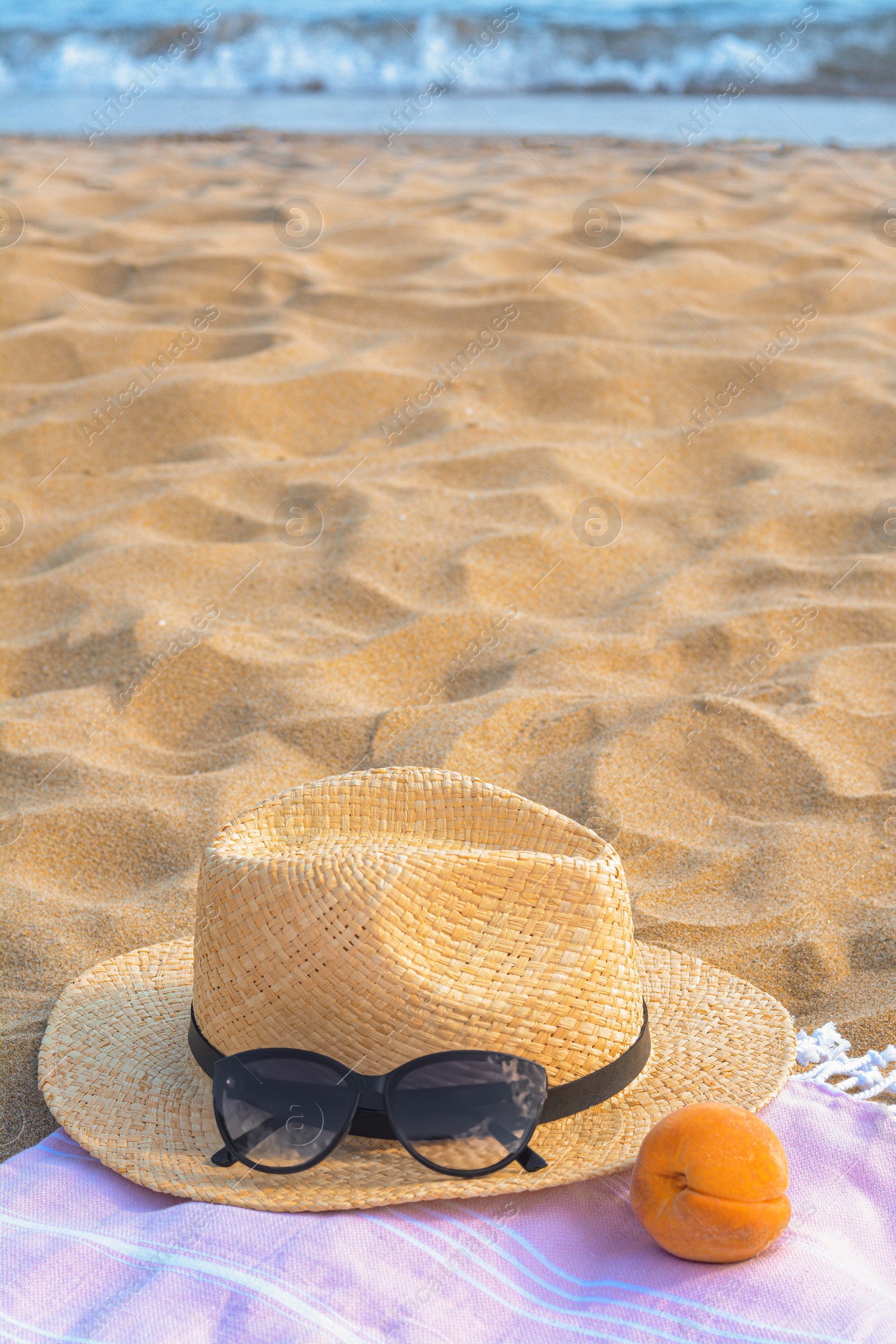 Photo of Hat with beautiful sunglasses and peach on sand near sea