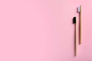 Two bamboo toothbrushes on pink background, flat lay. Space for text