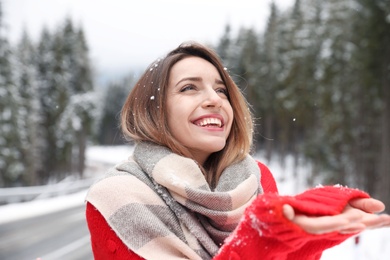 Photo of Young woman in warm clothes catching snow outdoors. Winter vacation