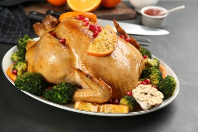 Photo of Delicious chicken with oranges, pomegranate and vegetables on black table, closeup