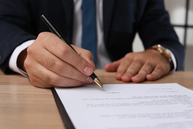 Photo of Businessman signing contract at wooden table indoors, closeup