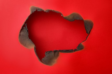 Photo of Burnt hole in paper on red background, space for text