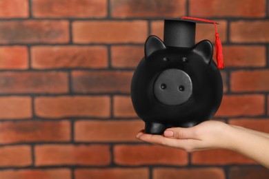 Photo of Woman holding piggy bank and graduation cap against brick background, closeup with space for text. Scholarship concept