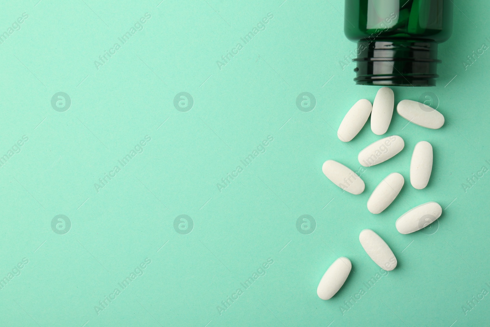 Photo of Vitamin pills and bottle on mint color background, top view. Space for text