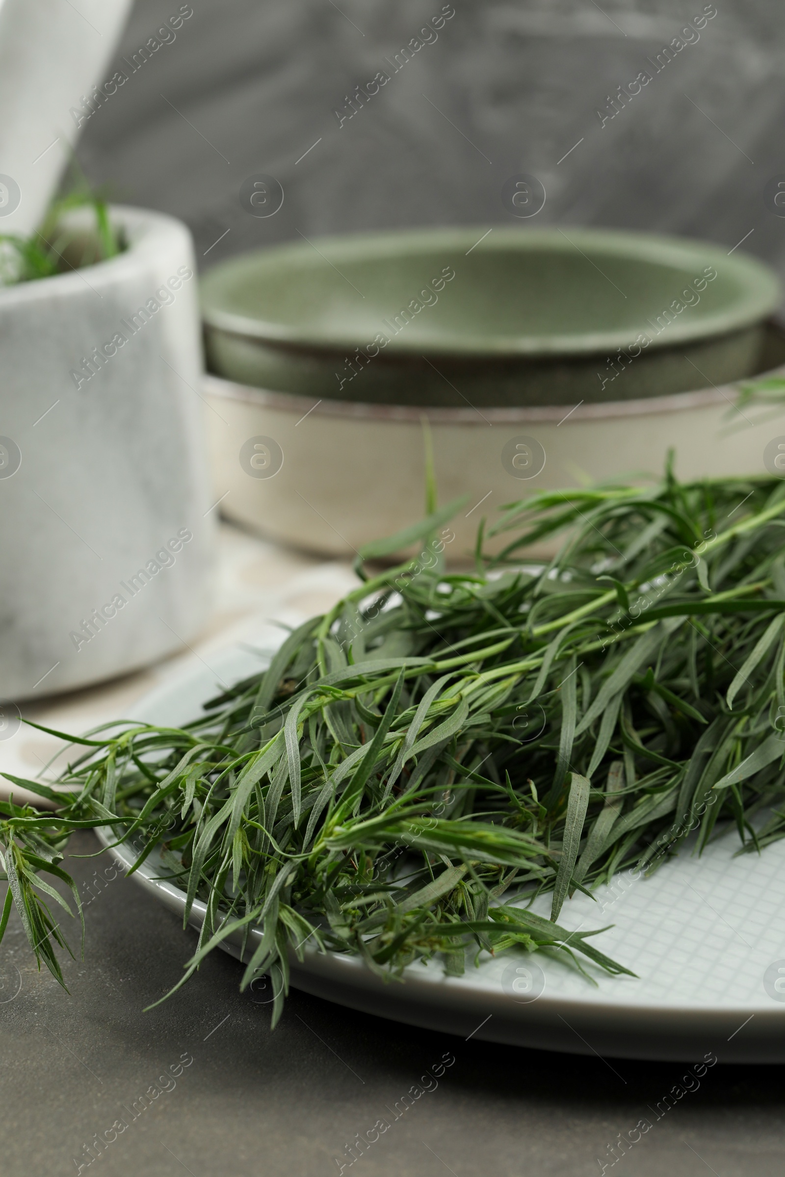 Photo of Plate with fresh tarragon leaves on grey table, closeup