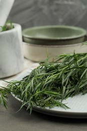 Photo of Plate with fresh tarragon leaves on grey table, closeup