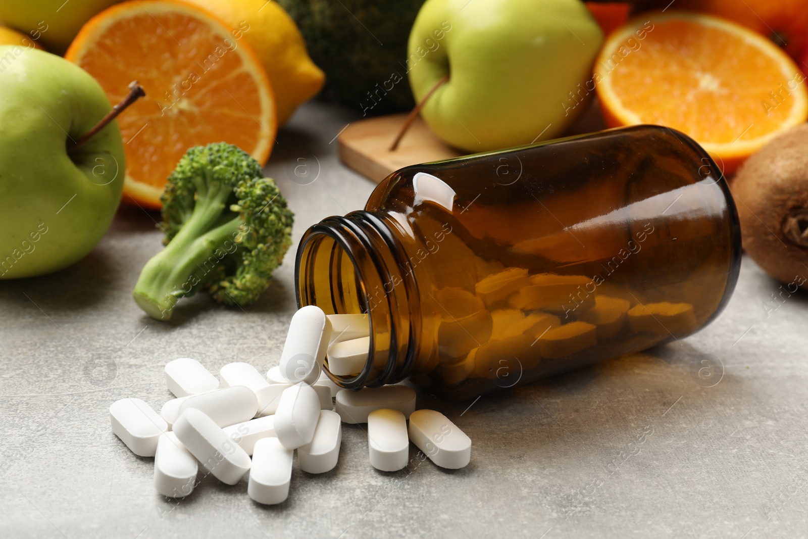 Photo of Dietary supplements. Overturned bottle, pills and food products on grey table