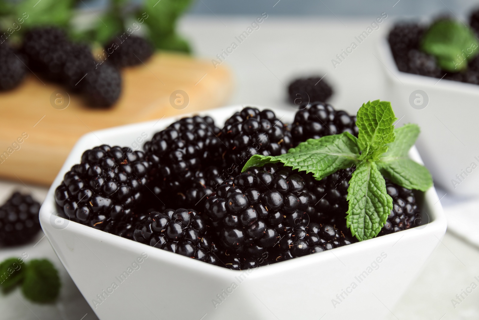 Photo of Bowl of tasty blackberries with mint on table, closeup