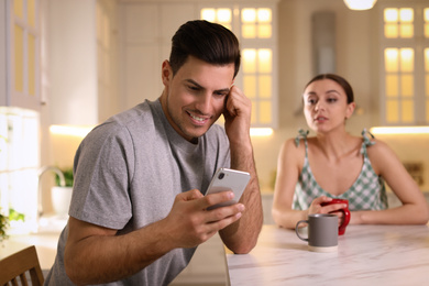 Photo of Distrustful woman peering into boyfriend's smartphone at home. Jealousy in relationship