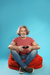 Emotional mature man playing video games with controller on color background. Space for text