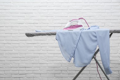 Photo of Modern iron and clean shirt on board against white brick wall