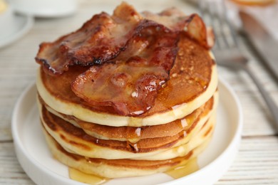 Delicious pancakes with maple syrup and fried bacon on white table, closeup