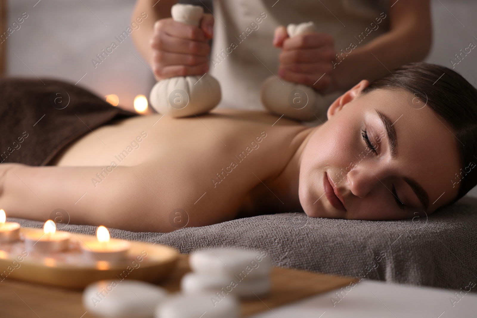 Photo of Spa therapy. Beautiful young woman lying on table during herbal bag massage in salon