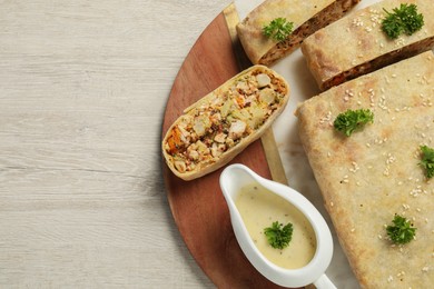 Photo of Cut tasty strudel with chicken, vegetables and sauce on light wooden table, top view. Space for text
