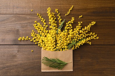 Beautiful mimosa flowers and envelope on wooden table, flat lay