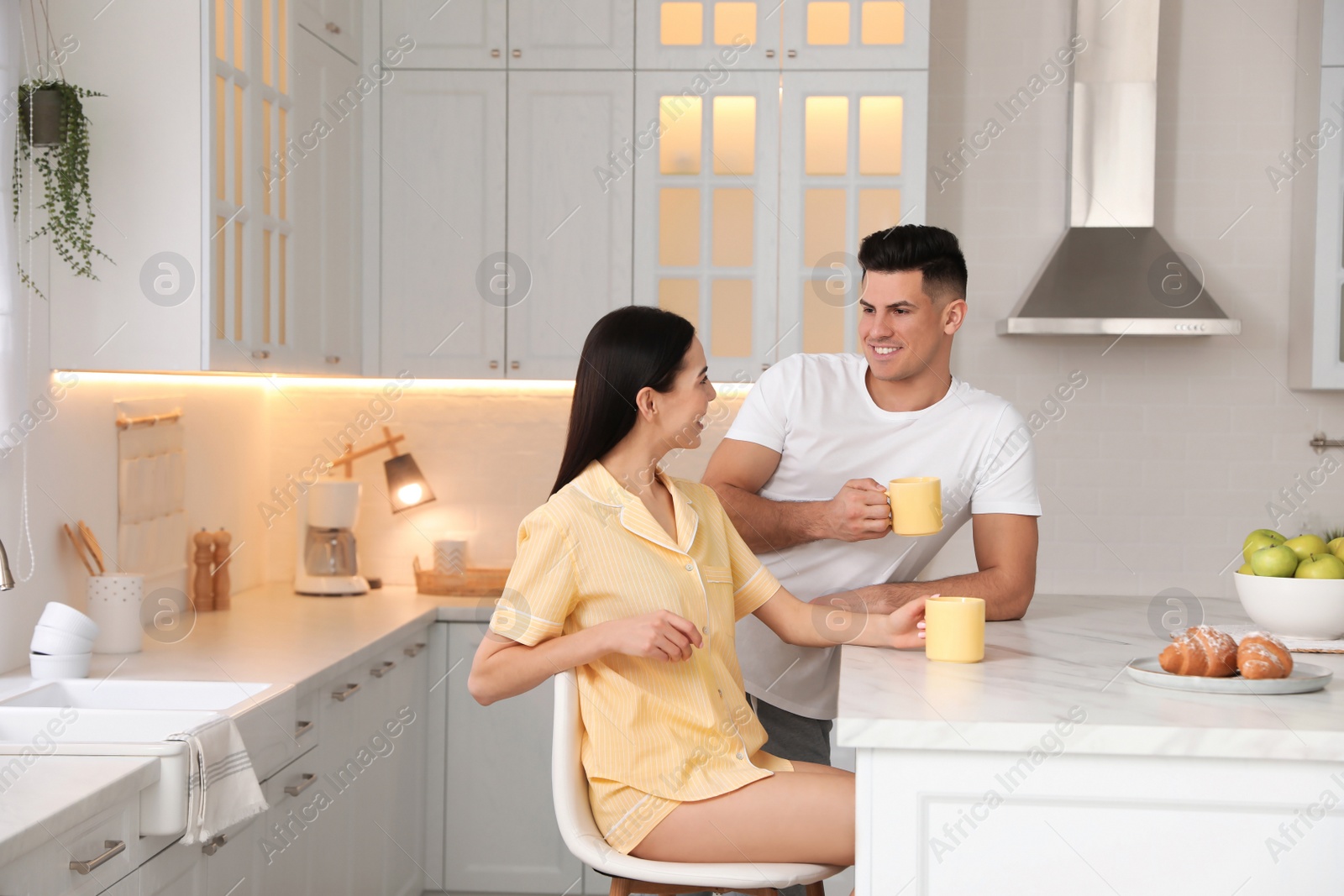 Photo of Happy couple wearing pyjamas during breakfast at table in kitchen