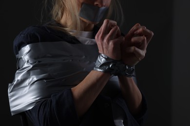 Photo of Woman taped up and taken hostage on dark background, closeup
