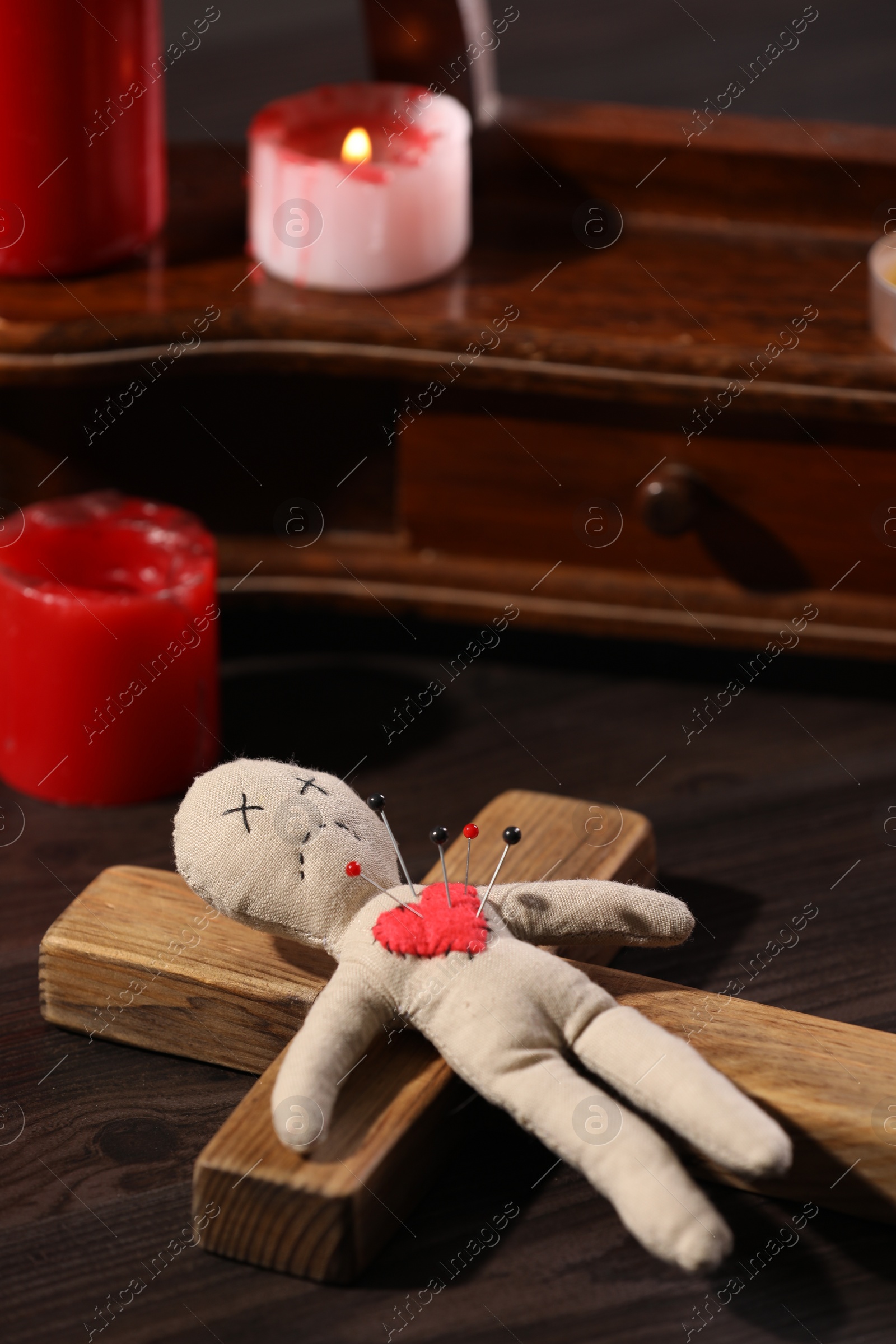 Photo of Voodoo doll with pins in heart and ceremonial items on wooden table