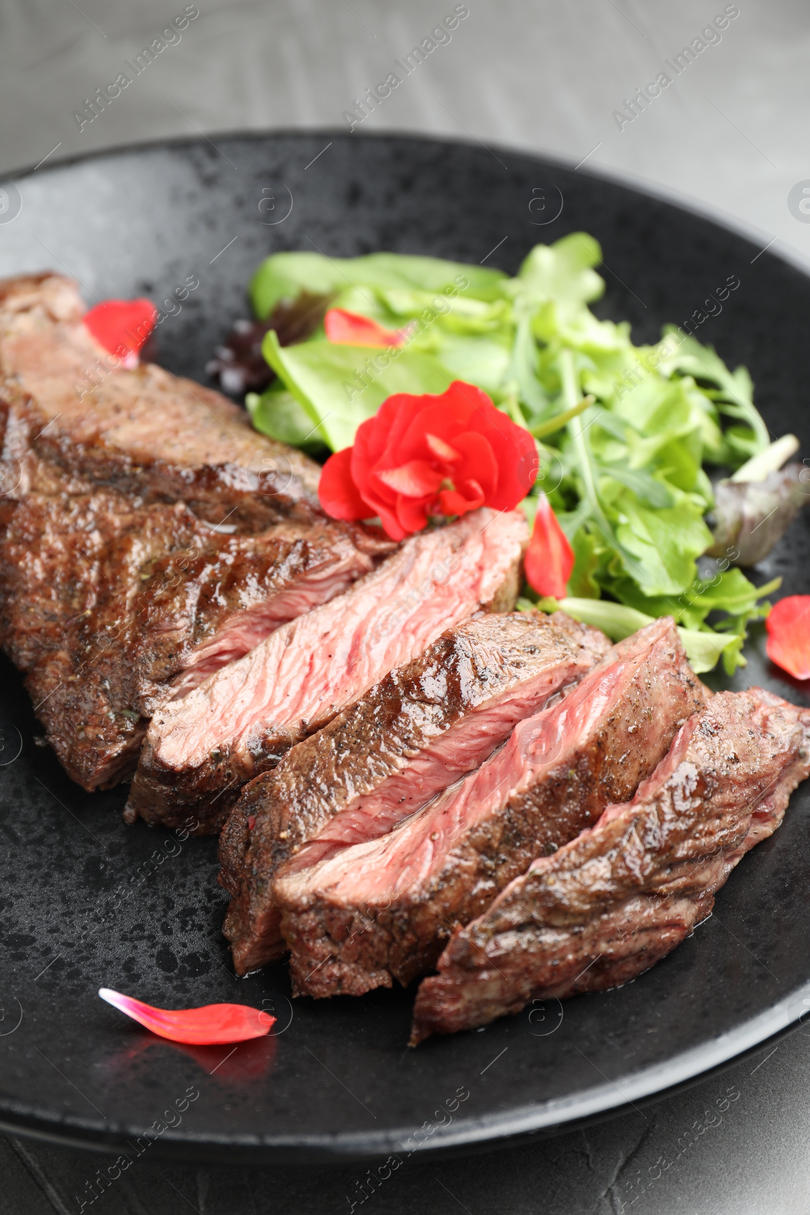 Photo of Pieces of delicious grilled beef meat and greens on table, closeup