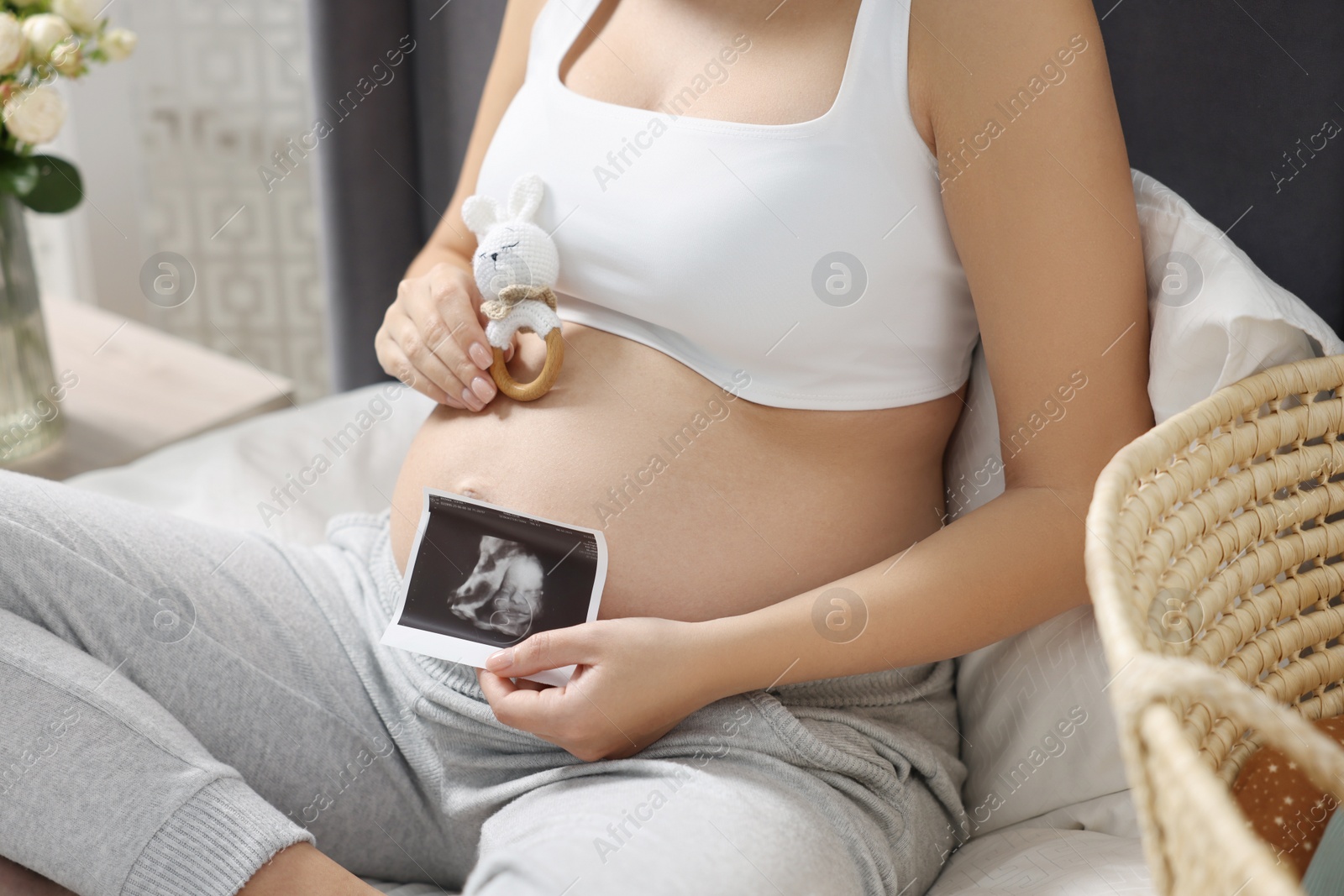 Photo of Pregnant woman with ultrasound picture of baby and bunny toy sitting on bed indoors, closeup