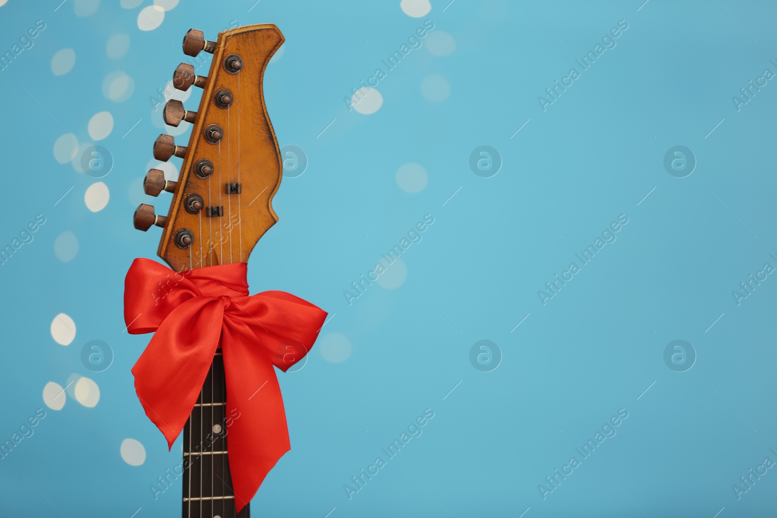 Photo of Guitar with red bow against blurred lights, space for text. Christmas music