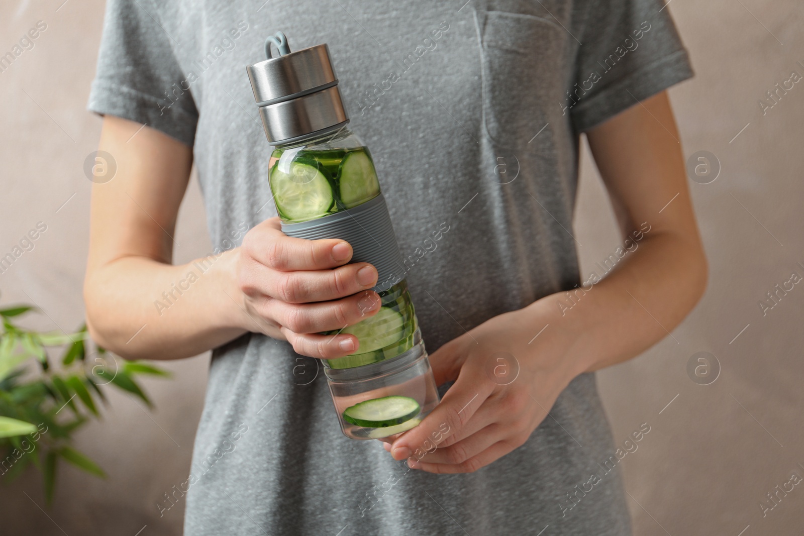 Photo of Young woman holding bottle with fresh cucumber water on color background, closeup