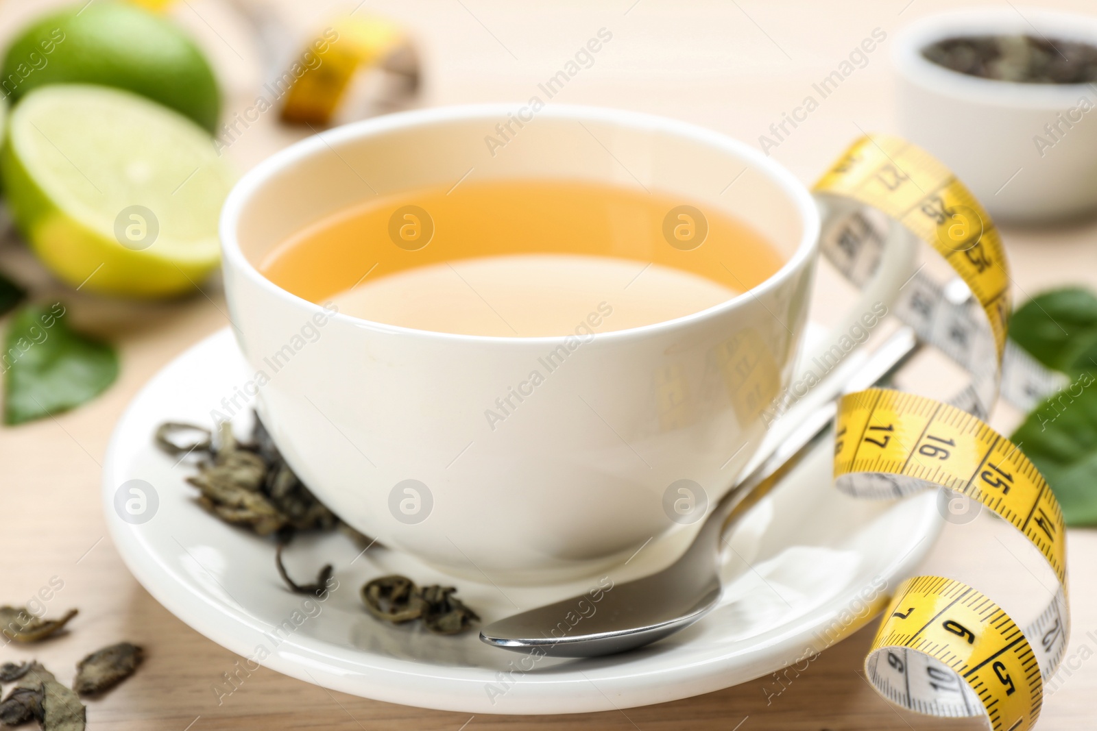 Photo of Cup of diet herbal tea, measuring tape and dried leaves on table, closeup