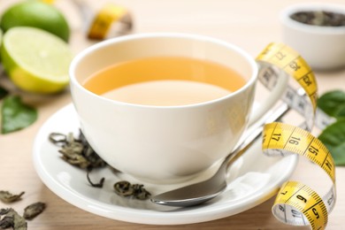 Cup of diet herbal tea, measuring tape and dried leaves on table, closeup