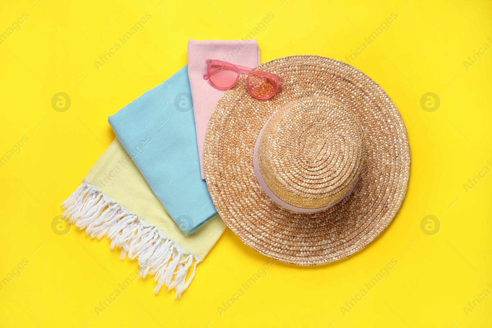 Photo of Beach towel, straw hat and sunglasses on yellow background, flat lay