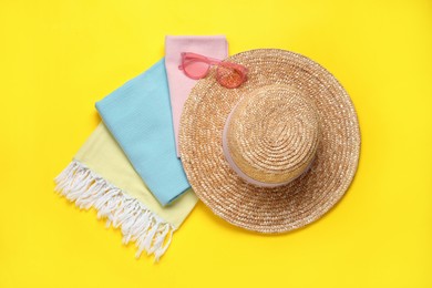 Beach towel, straw hat and sunglasses on yellow background, flat lay