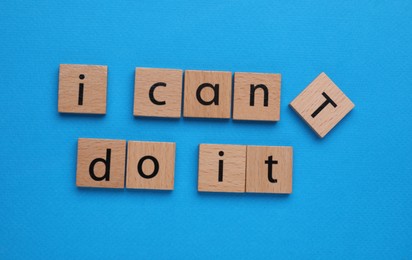 Photo of Motivation concept. Changing phrase from I Can't Do It into I Can Do It by removing wooden square with letter T on light blue background, flat lay
