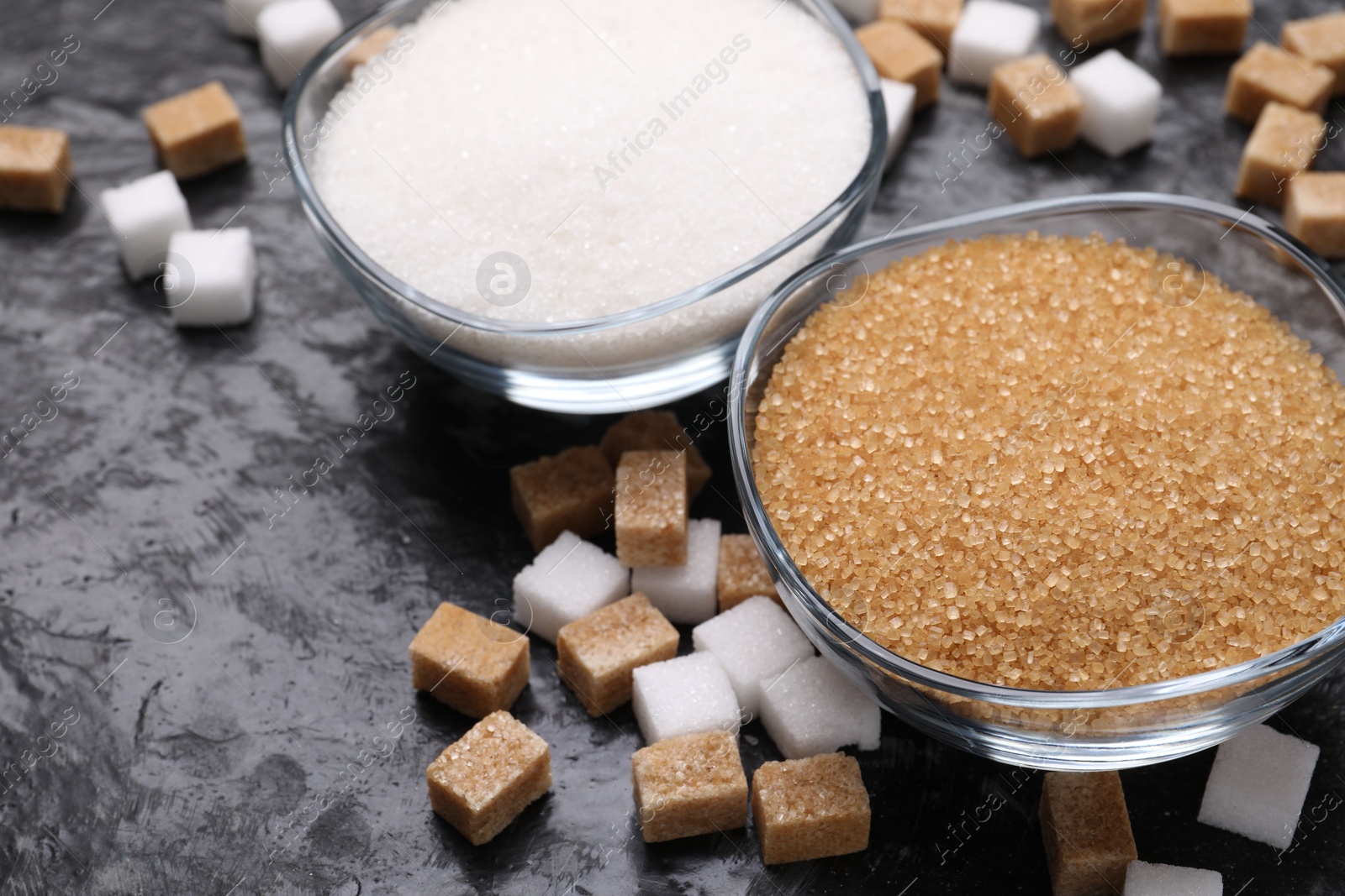 Photo of Different types of sugar in bowls on dark gray textured table, closeup