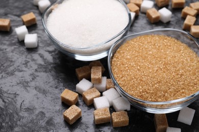 Different types of sugar in bowls on dark gray textured table, closeup