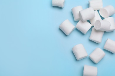 Photo of Delicious puffy marshmallows on light blue background, flat lay. Space for text
