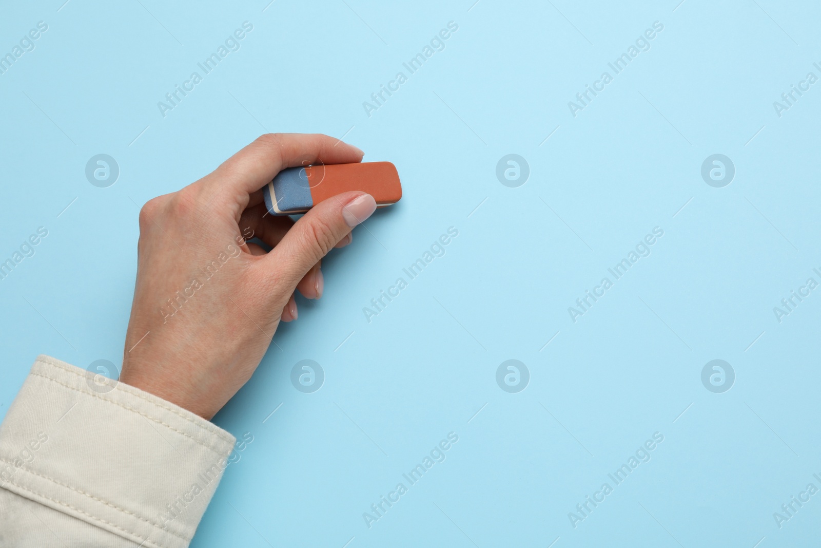 Photo of Woman erasing something on light blue background, closeup. Space for text