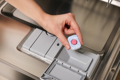 Woman putting detergent tablet into open dishwasher, closeup