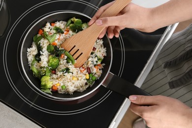 Photo of Woman frying rice with vegetables on induction stove, top view