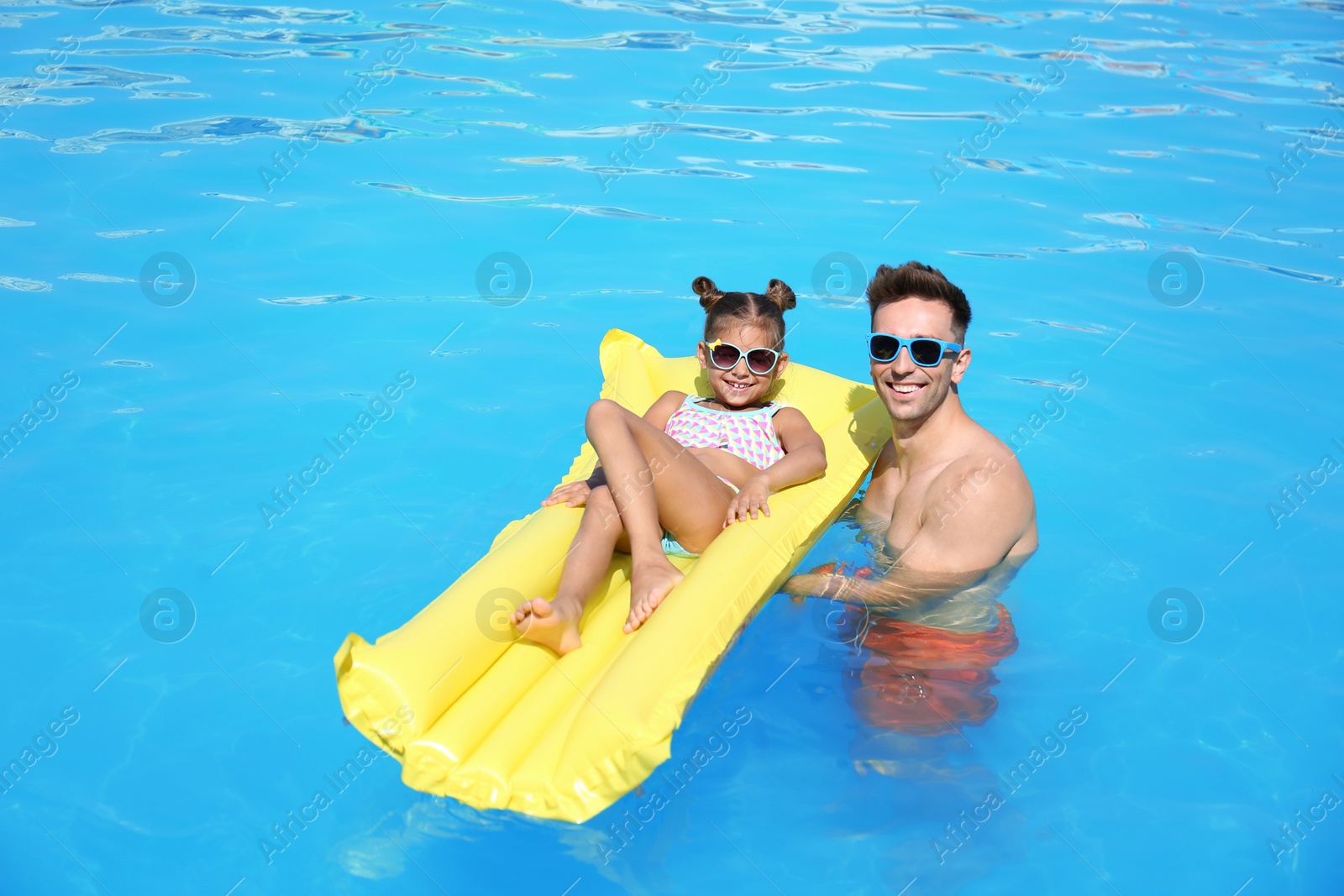 Photo of Little girl on inflatable mattress with father in swimming pool
