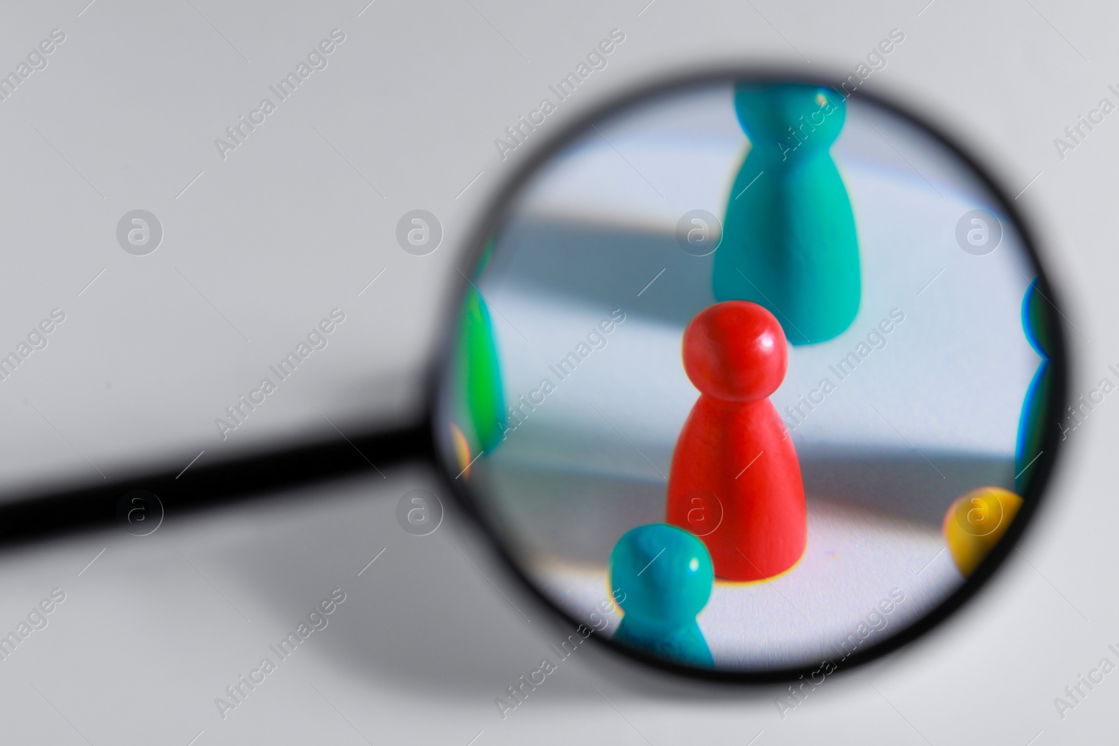 Photo of Magnifying glass over colorful pawns on white background. Recruiter searching employee