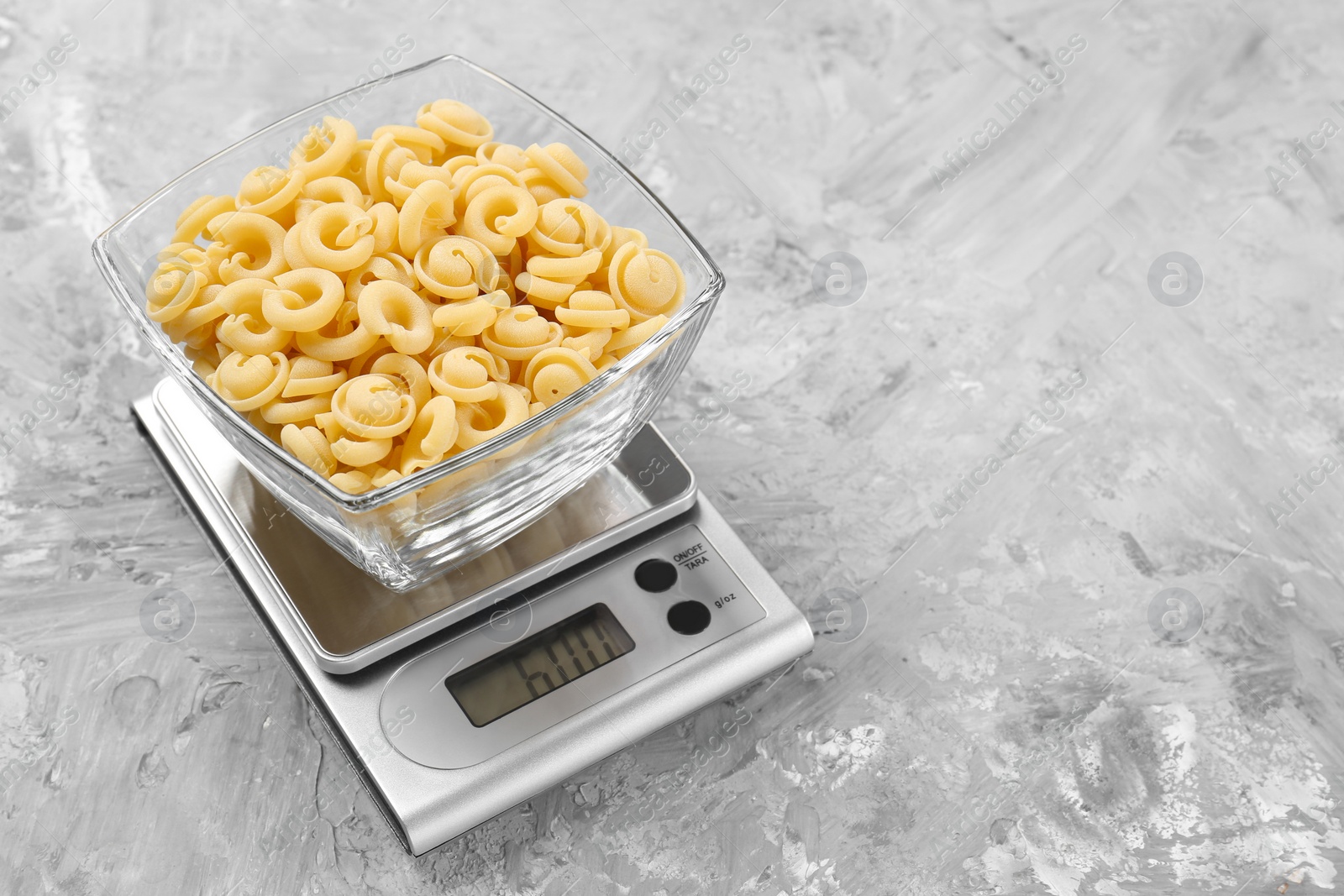 Photo of Kitchen scale with bowl of pasta on grey textured table. Space for text