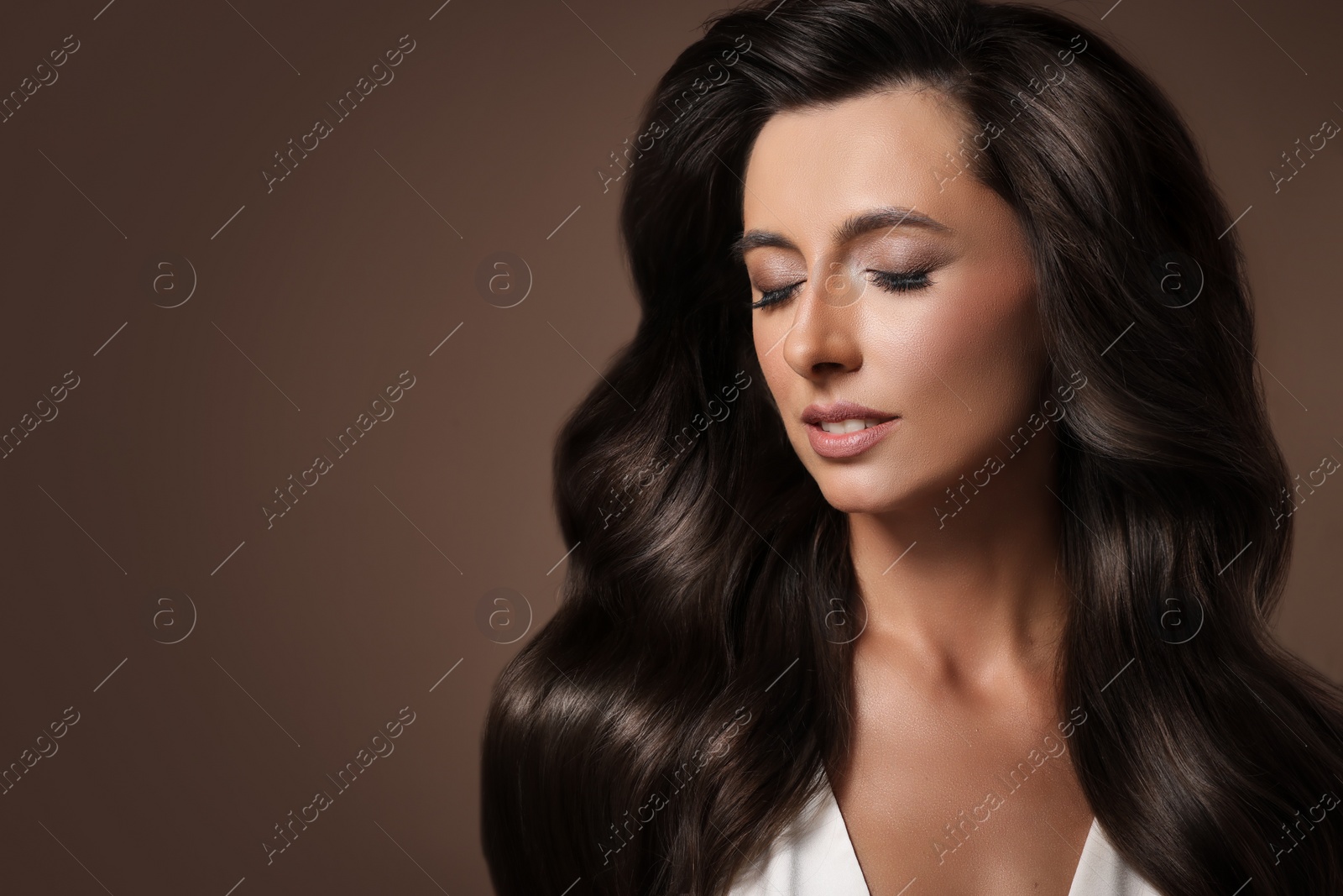 Image of Gorgeous woman with shiny wavy hair on brown background, space for text. Professional hairstyling