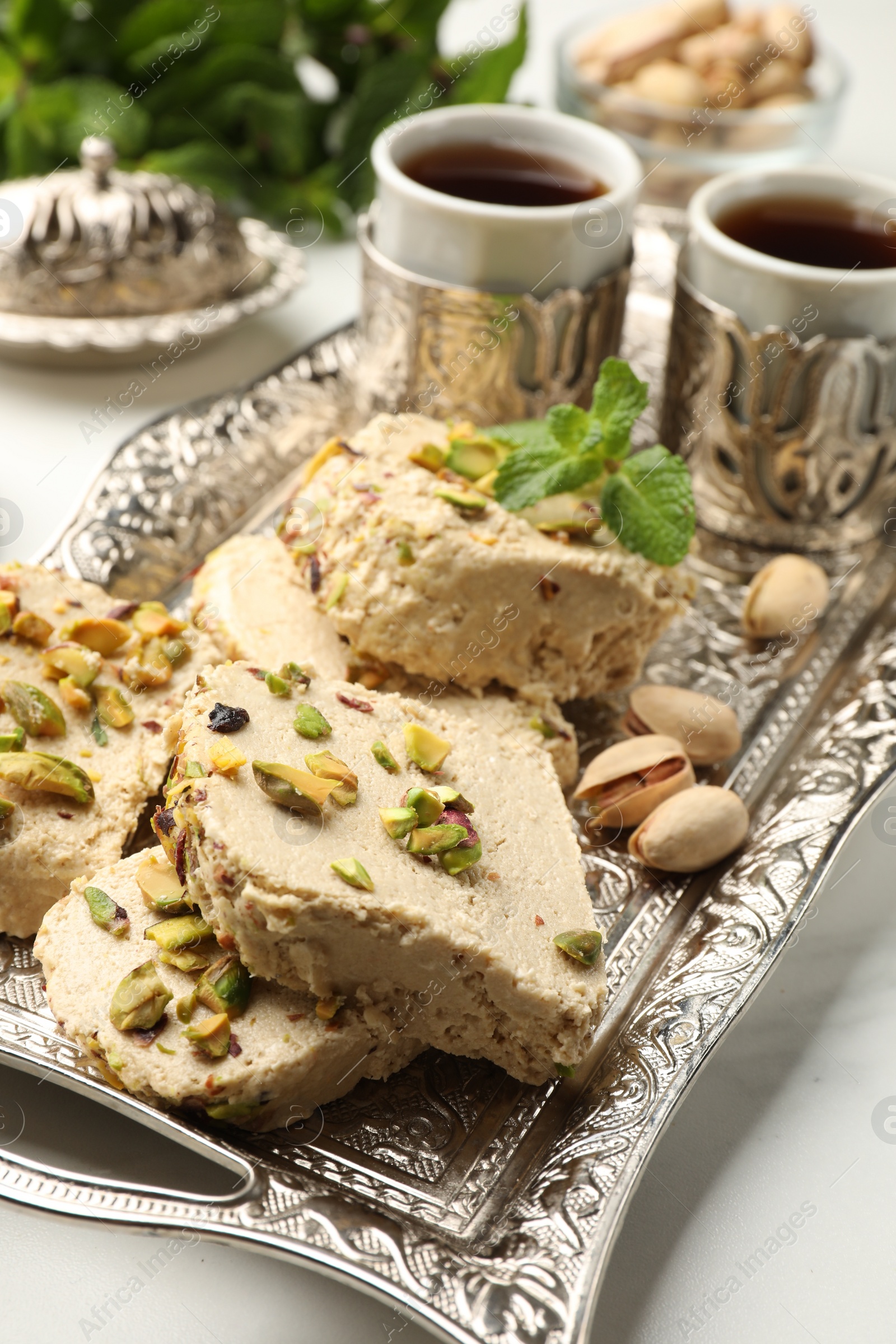 Photo of Tasty halva with pistachios and mint served on white table, closeup