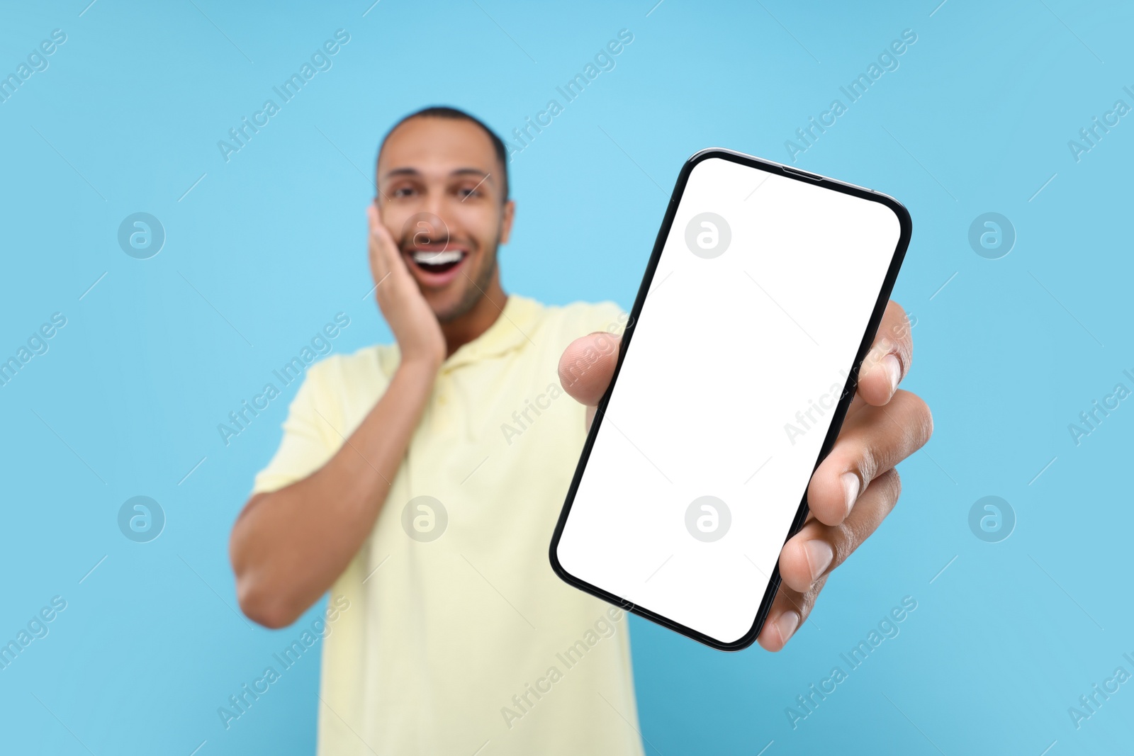 Photo of Surprised man showing smartphone in hand on light blue background, selective focus. Mockup for design