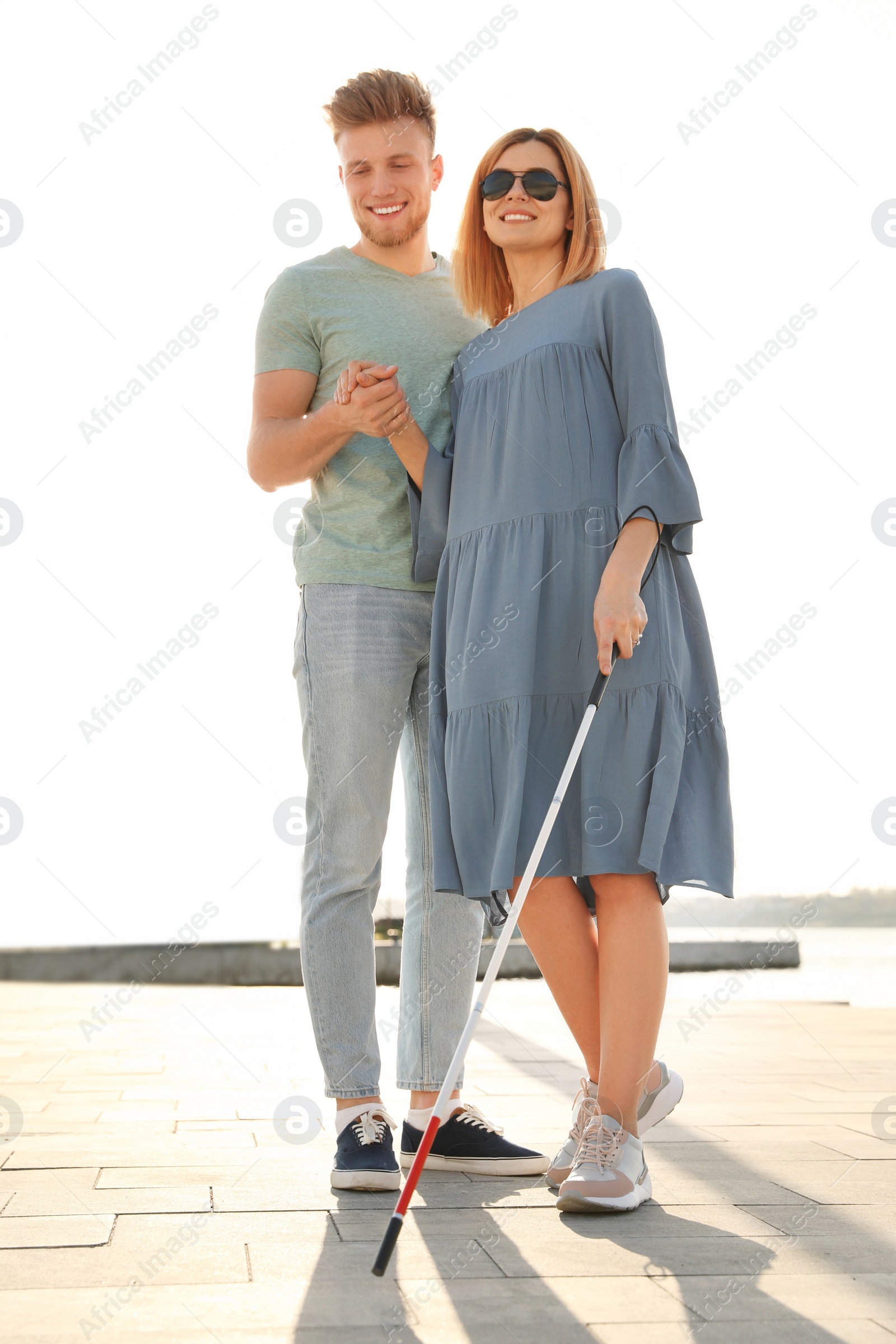 Photo of Young man helping blind person with long cane in city