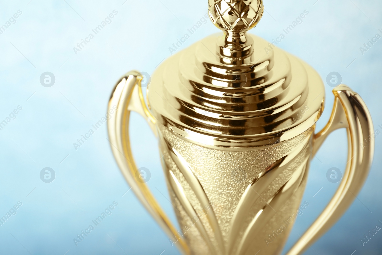 Photo of Shiny golden trophy cup on blue background, closeup