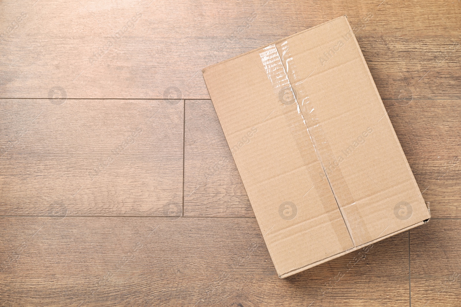 Photo of Cardboard box on wooden floor, top view. Space for text