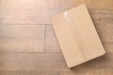 Cardboard box on wooden floor, top view. Space for text