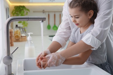 Photo of Mother and daughter washing hands with liquid soap together in kitchen, closeup
