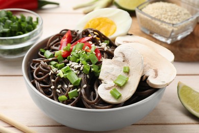 Photo of Tasty buckwheat noodles (soba) with mushrooms, onion, egg and chili pepper in bowl on wooden table, closeup